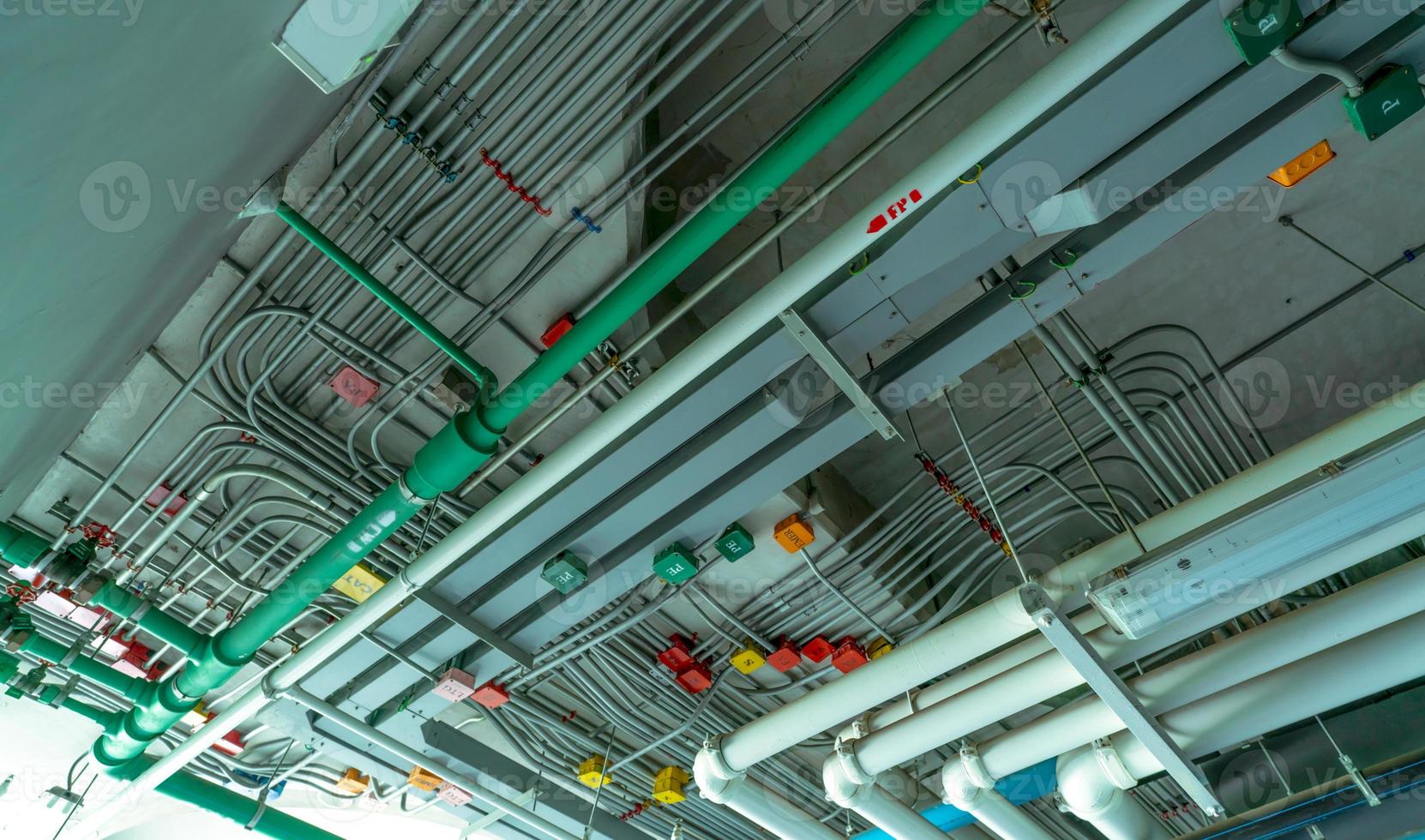 Electrical conduit system and galvanized steel pipe of electric cable installed on ceiling. PVC plastic pipe of drainage system and clean water on industrial building ceiling. Building construction. photo