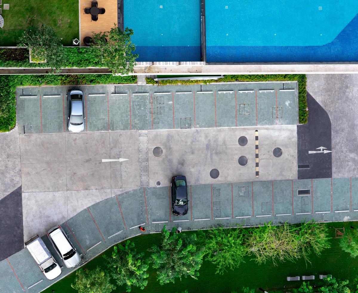 Top view concrete car parking lot, swimming pool, and garden of apartment. Aerial view of car parked at car parking area of condo. Outdoor parking space with empty slot. One way traffic sign on road. photo