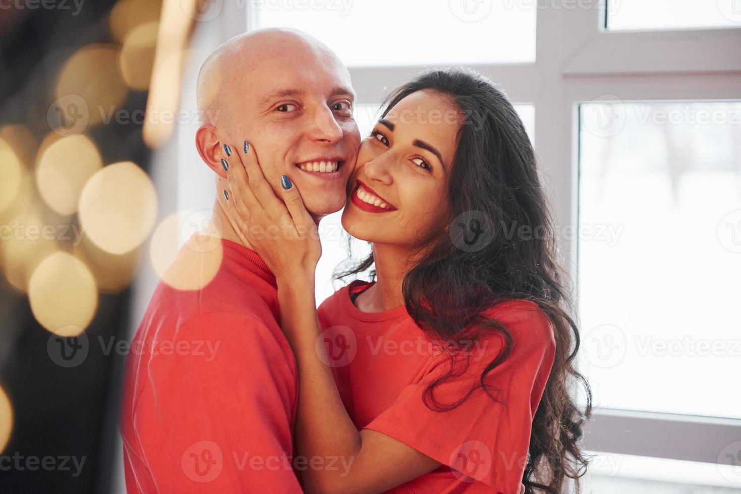 Feels awesome to be together. Cheerful couple standing near the window, smiling and looking into the camera photo