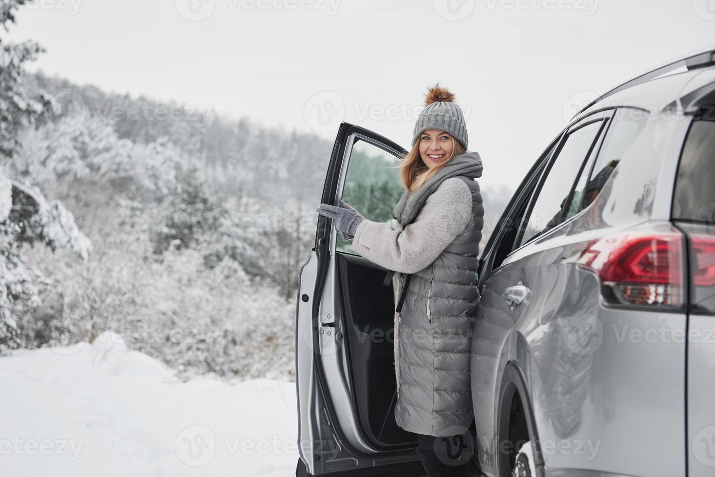 Lovely day. Woman walks out from the modern car to have a walk in the nice winter forest photo