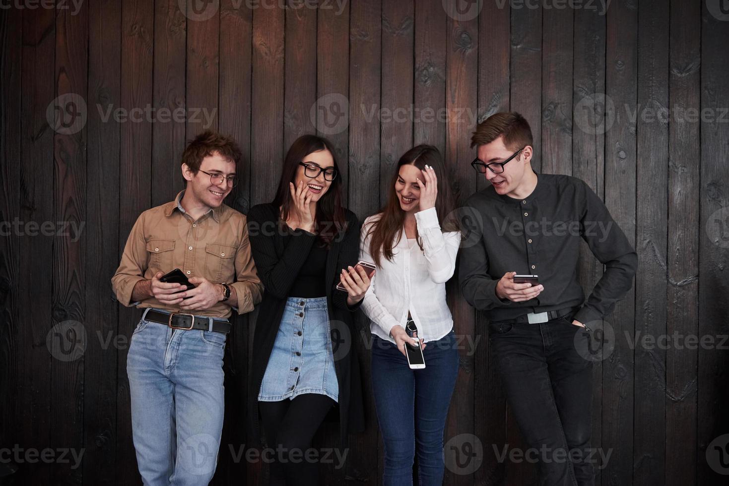 bromeando el joven se para contra la pared de madera negra. grupo de amigos pasando tiempo juntos foto