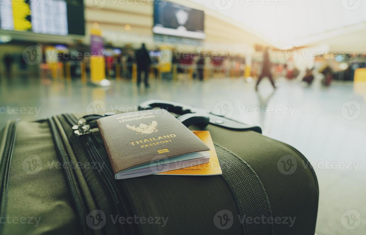 Thailand passport and vaccine passport on baggage on blur background of tourist in the airport. Certificate of vaccination for travel during coronavirus outbreak. Thai words are Thailand passport. photo