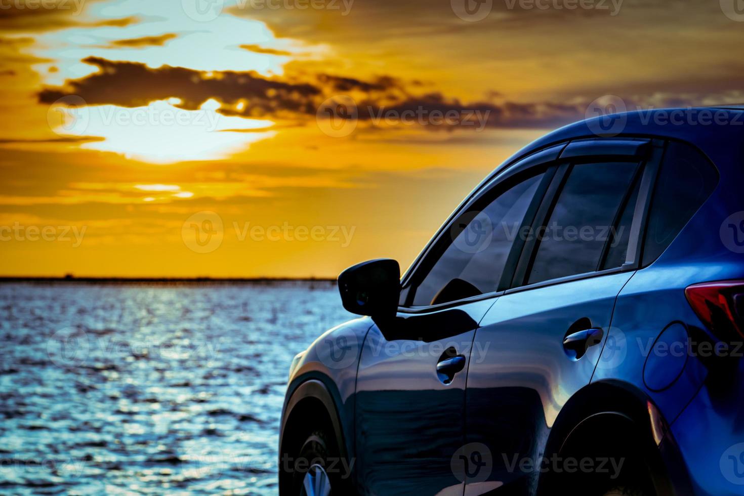 Blue compact SUV car with sport and modern design parked on concrete road by the sea at sunset. Environmentally friendly technology. Electric car technology and business. Hybrid auto and automotive. photo