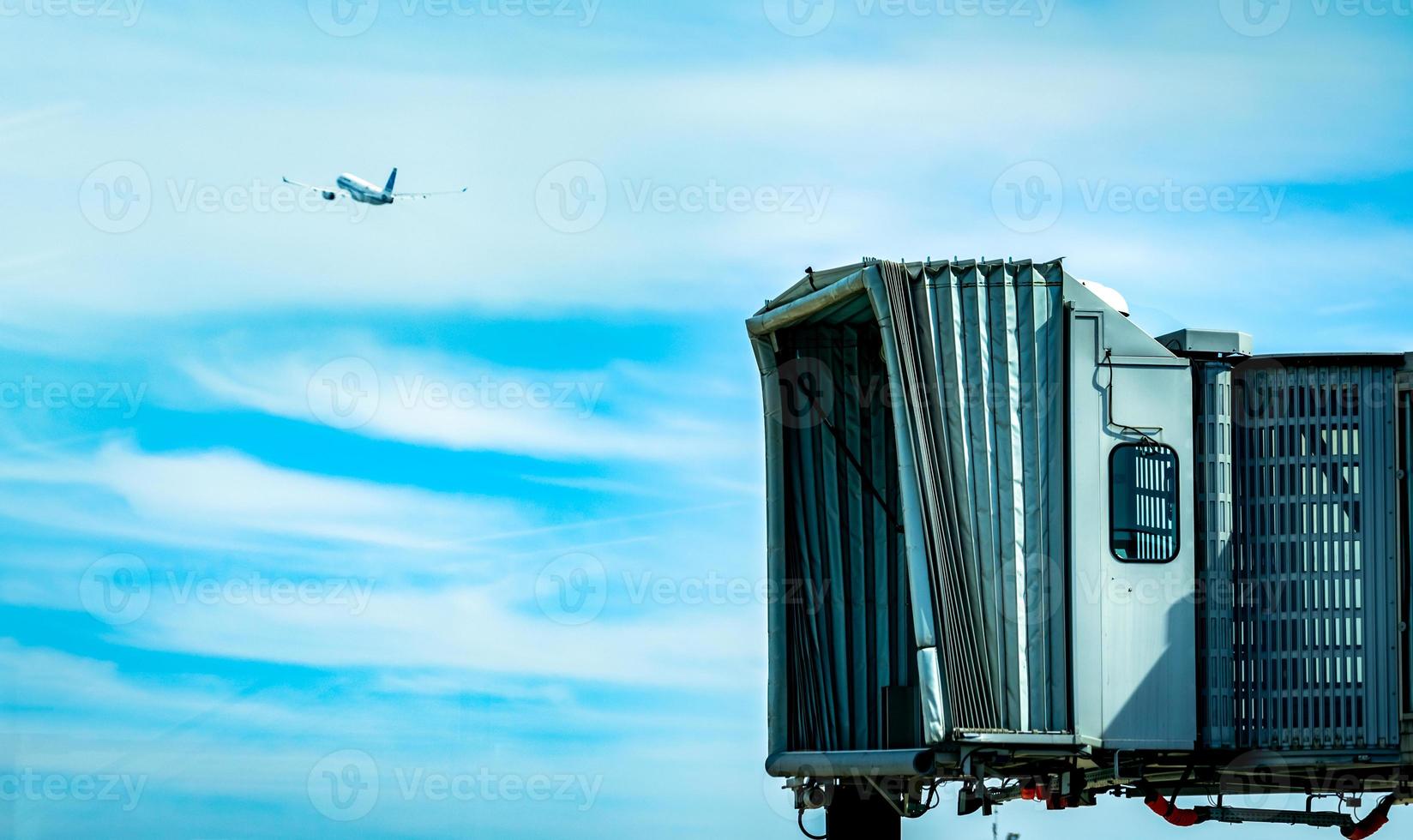 Jet bridge after commercial airline take off at the airport and the plane flying in the blue sky and white clouds. Aircraft passenger boarding bridge docked. Departure flight of international airline. photo