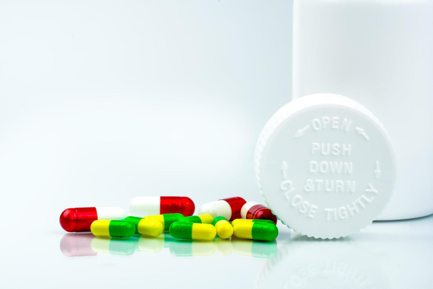Colorful pills on white background and plastic bottle with blank label and copy space. Childproof packaging. Child resistant pill container. Push down and turn cap.Global healthcare concept. photo