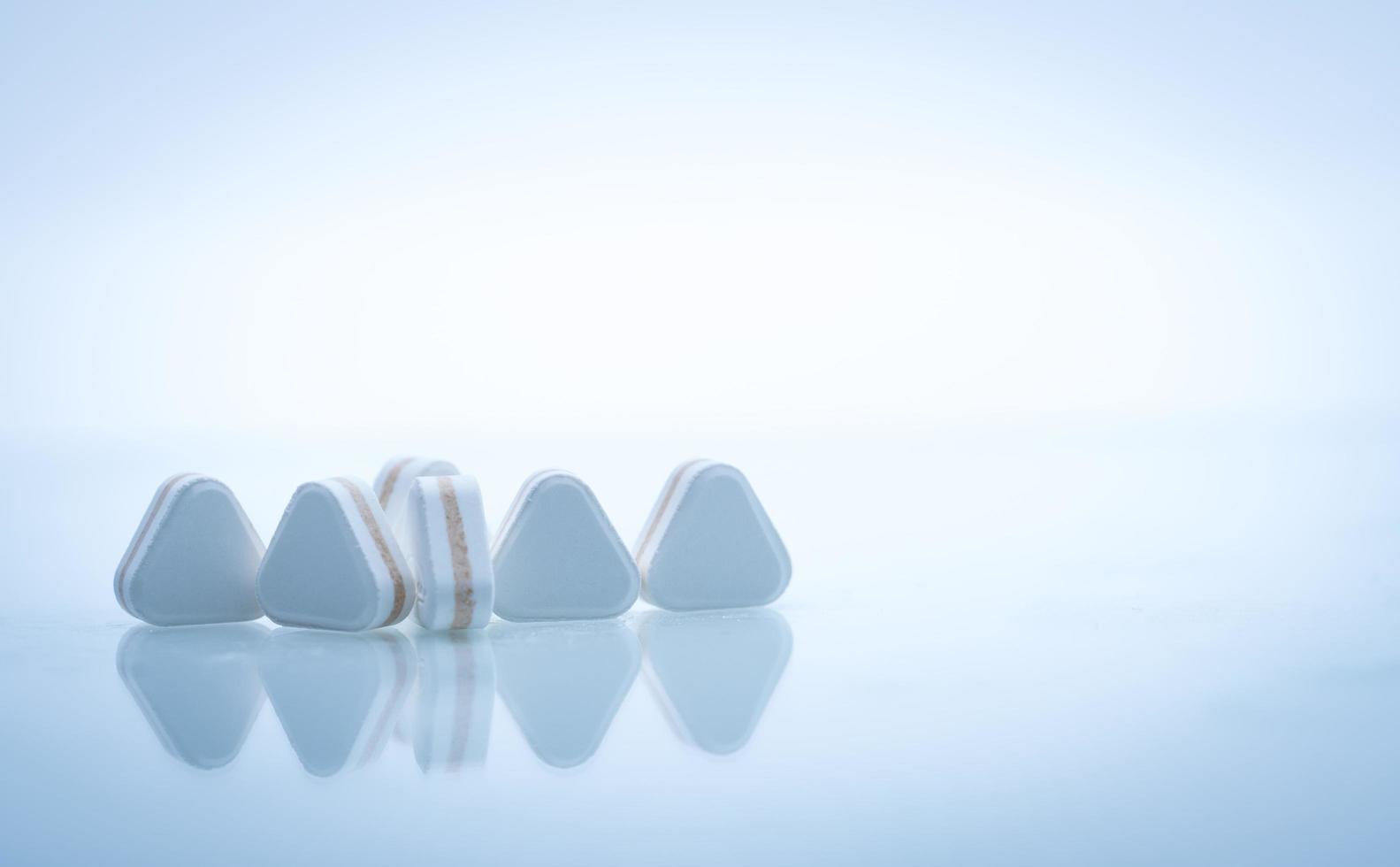 Macro shot of triangle shape tablet pills. Three layers tablet pills for indication antacid, digestive and gastric pain. Group of sandwich tablets pills on white background with copy space for text. photo