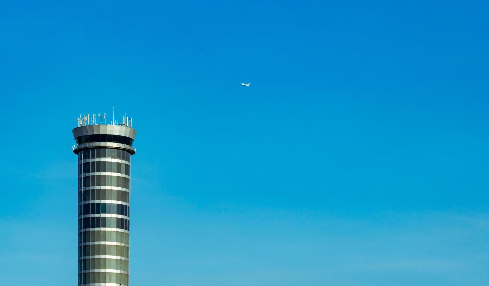 torre de control de tráfico aéreo en el aeropuerto con avión de vuelo internacional volando en un cielo azul claro. torre de control de tráfico del aeropuerto para el control del espacio aéreo por radar. tecnología de la aviación. gestión de vuelos. foto