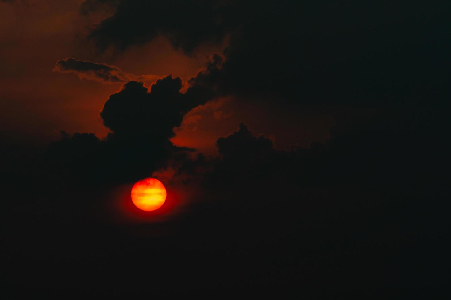 Red big sun in dark clouds. Devil sunset. Horror view of sun in black clouds sky. Summer sunset. Fiery sun in the evening. Nature background. Dramatic sky with big sun. Heat weather. Heaven concept. photo
