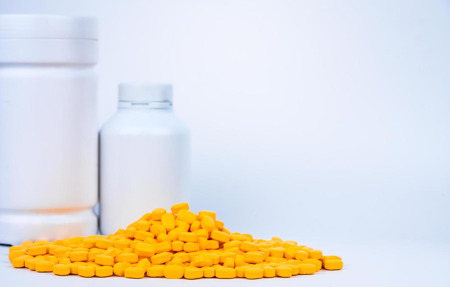 Pile of yellow tablets pills near plastic pills bottle with blank label isolated on white background with copy space. Ibuprofen for relief pain, headache, high fever and anti-inflammatory. Painkiller photo