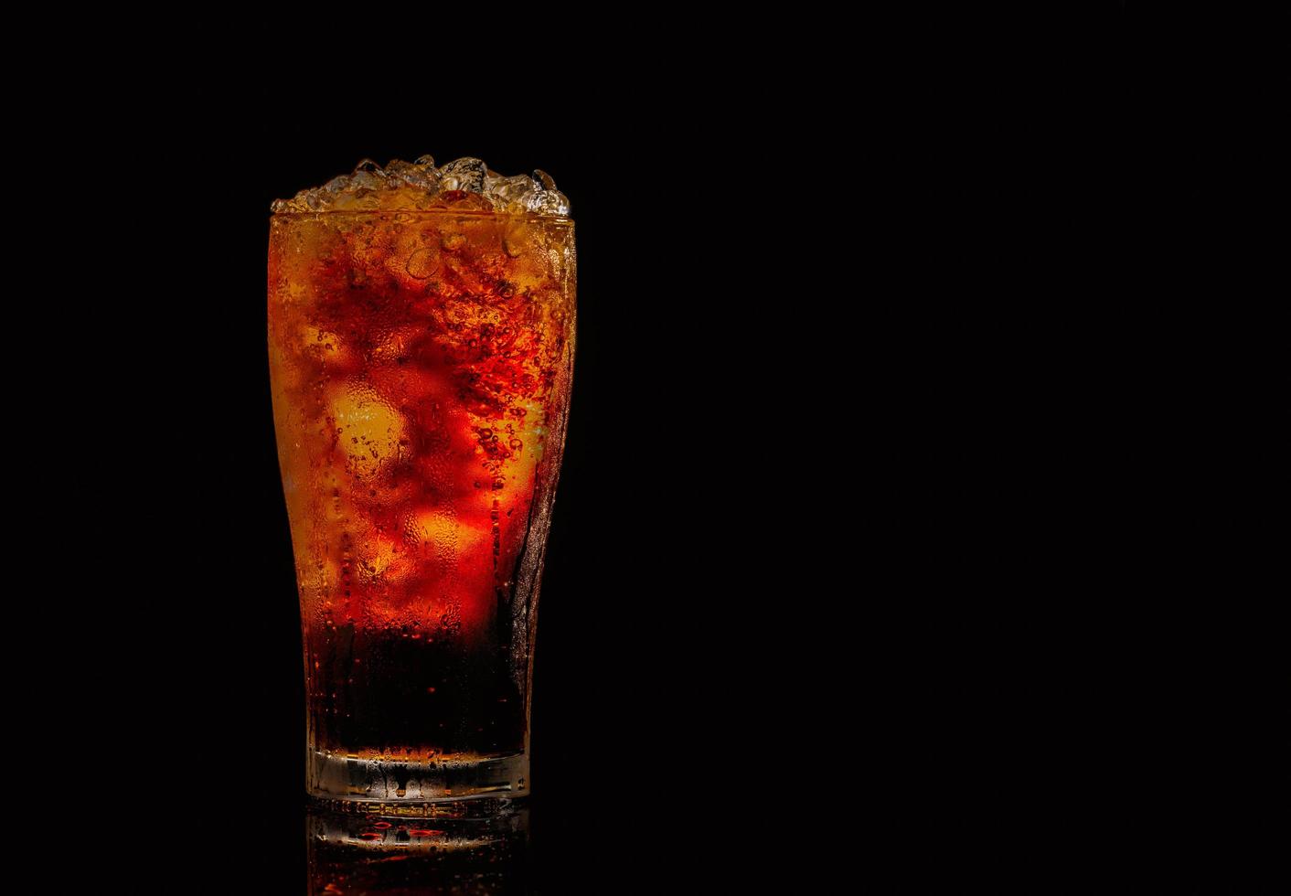 refresco con cubitos de hielo picado en vidrio aislado sobre fondo oscuro con espacio de copia. hay una gota de agua en la superficie de vidrio transparente. foto