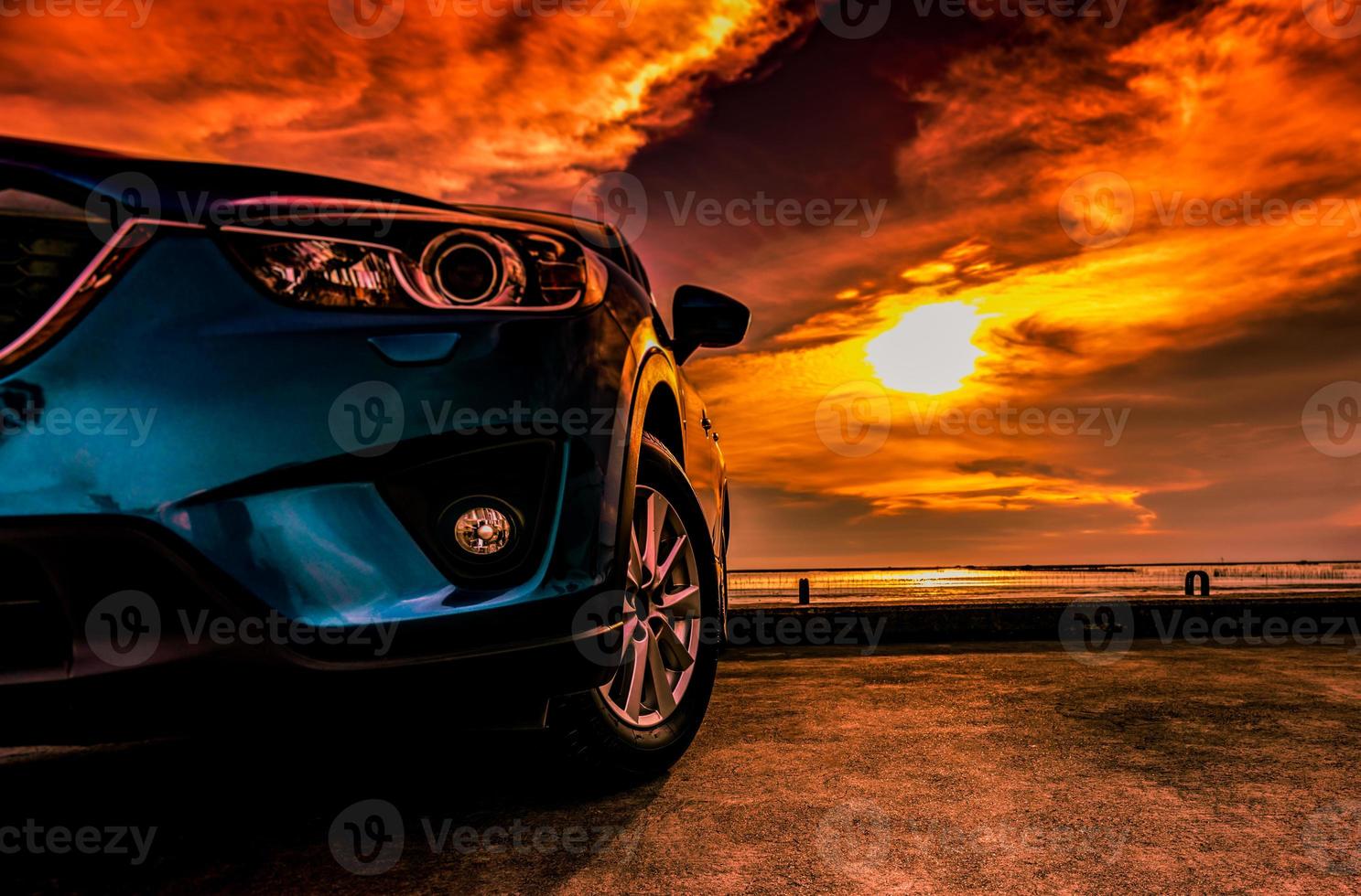 Blue compact SUV car with sport, modern, and luxury design parked on concrete road by the sea at sunset. Front view of beautiful hybrid car. Driving with confidence. Travel on vacation at the beach. photo