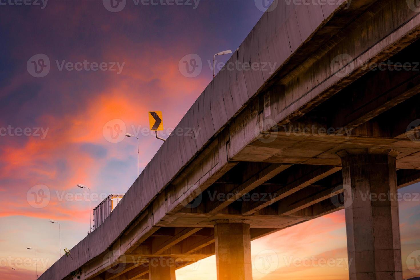 Bottom view of elevated concrete highway. Overpass concrete road. Road flyover structure. Motorway with red sunrise sky. Concrete bridge engineering construction. Bridge architecture. Infrastructure. photo