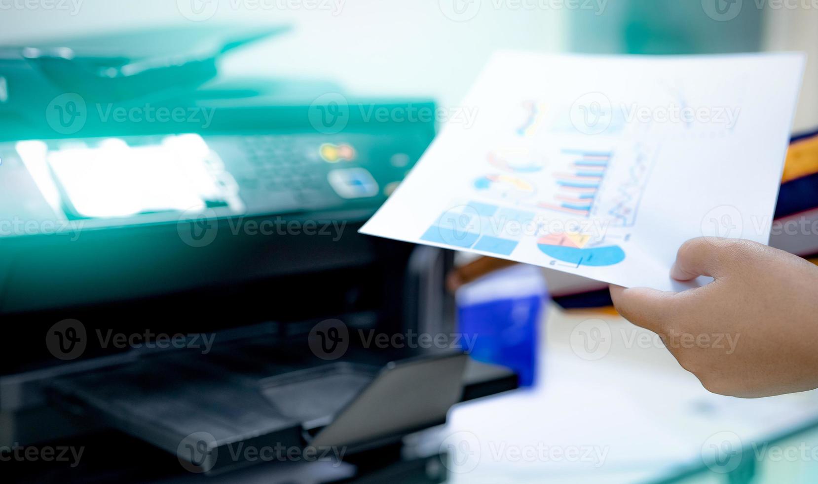 Selective focus on office worker hand holding paper. Multifunction laser printer. Copy, print, scan, and fax machine in office. Modern print technology. Photocopy machine. Document and paper work. photo