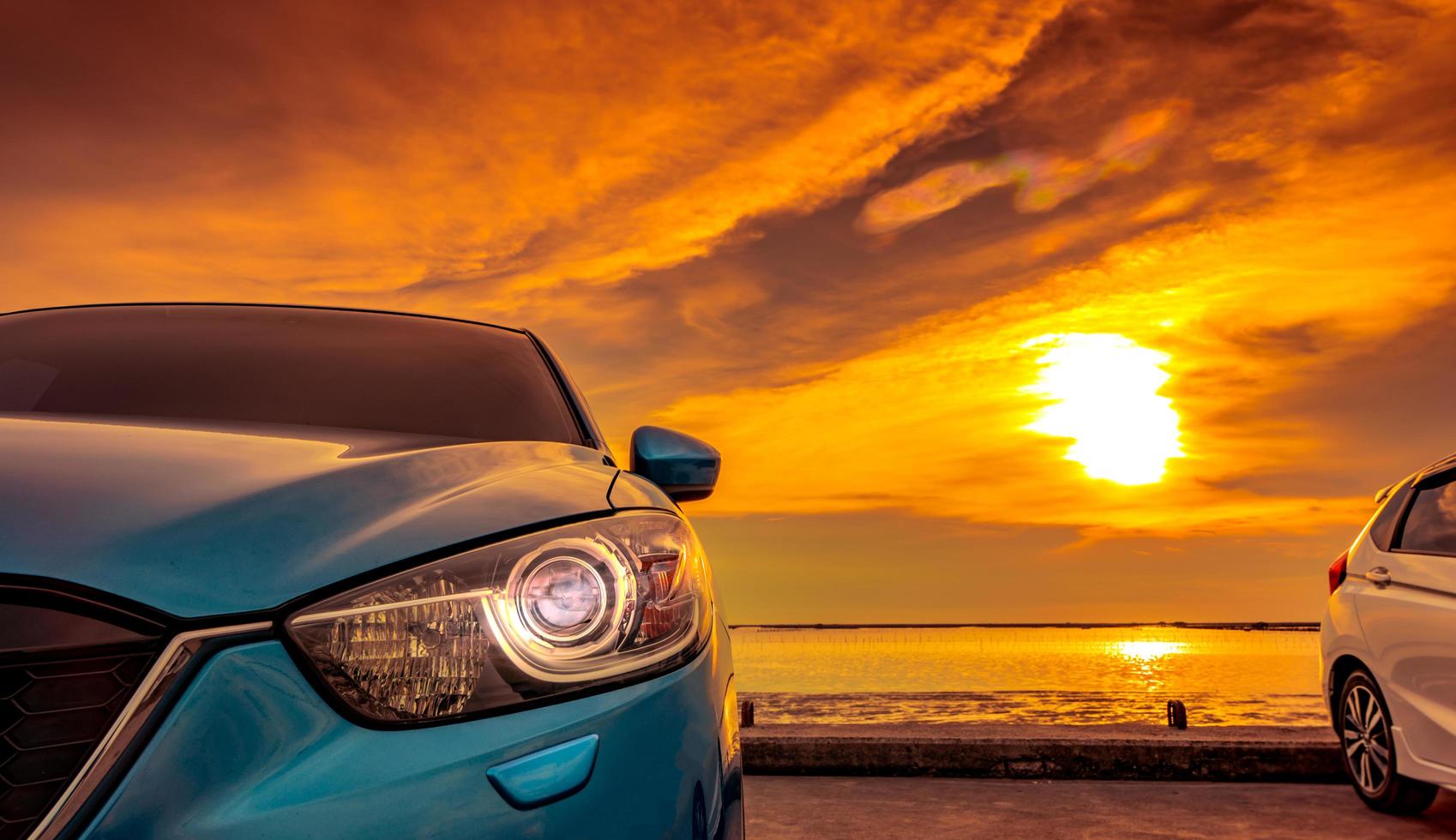 Blue and white compact SUV car with sport and modern design parked on concrete road by the sea at sunset. Environmentally friendly technology. Business success concept. Car with open headlamp light. photo