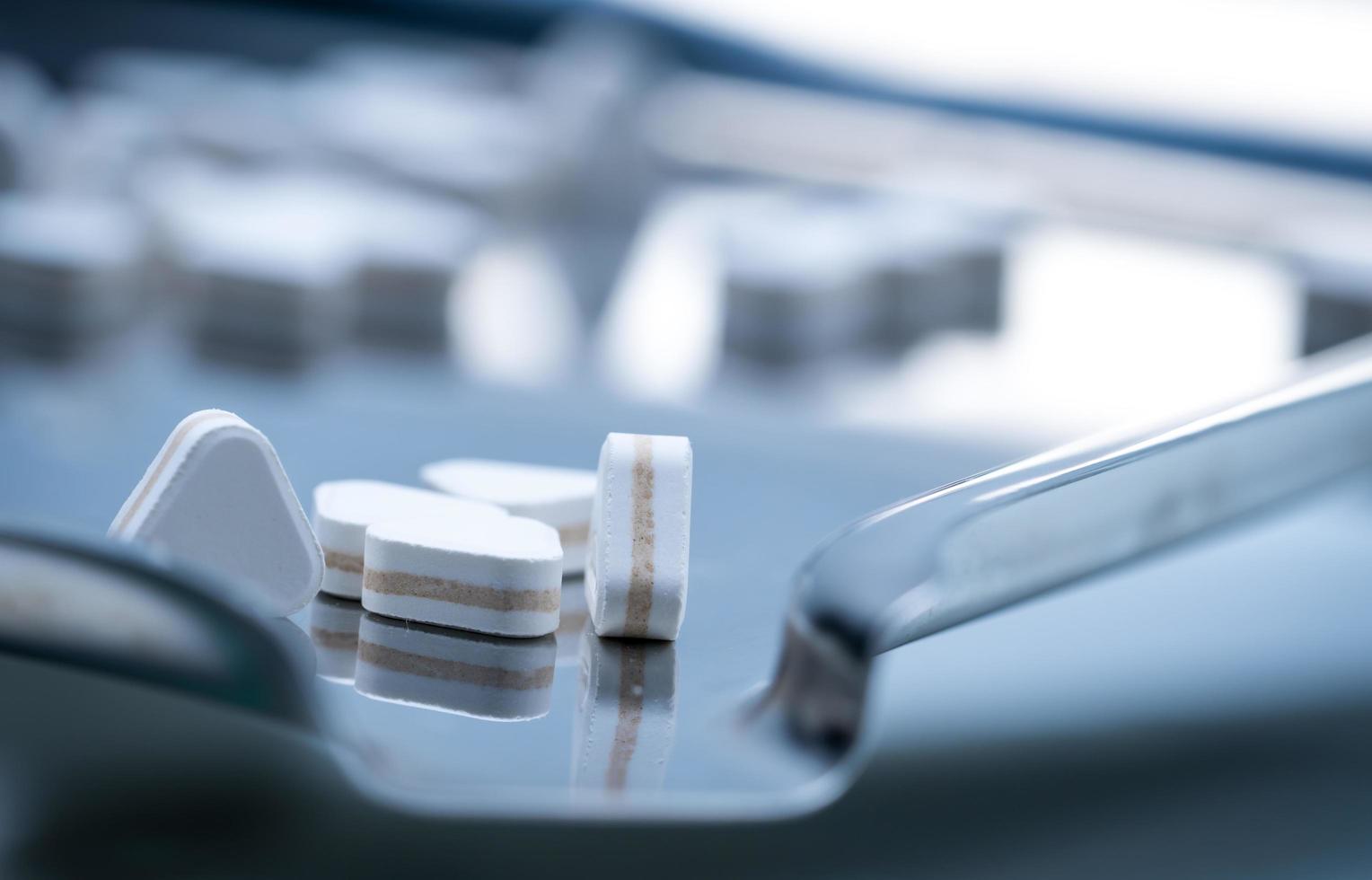 Macro shot of triangle shape tablet pills. Three layers tablet pills for indication antacid, digestive and gastric pain. Group of sandwich tablets pills on stainless steel drug tray. photo