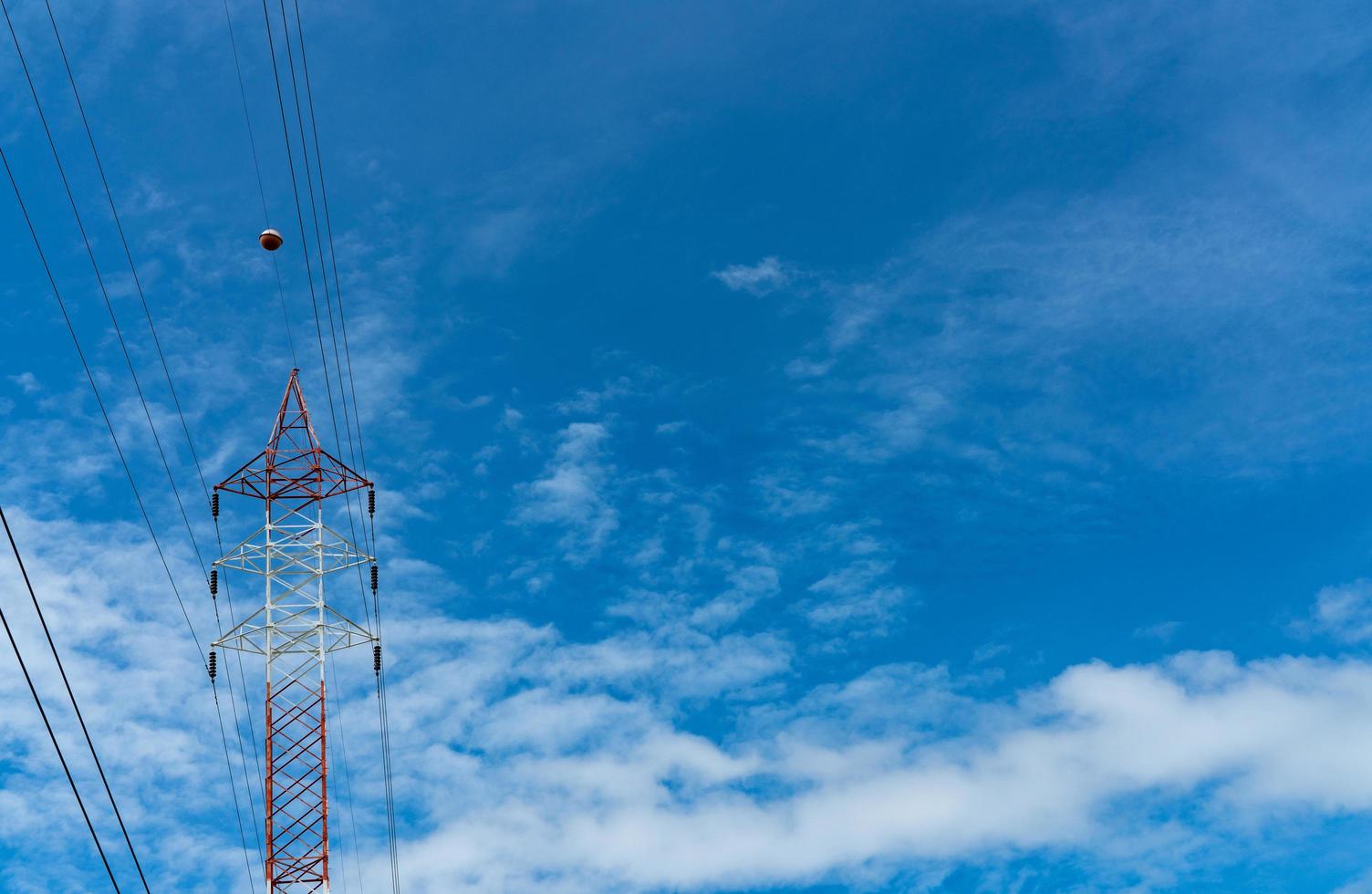 High voltage electric tower and transmission lines. Electricity pylon with blue sky and white clouds. Power and energy conservation. High voltage grid tower with wire cable at distribution station. photo