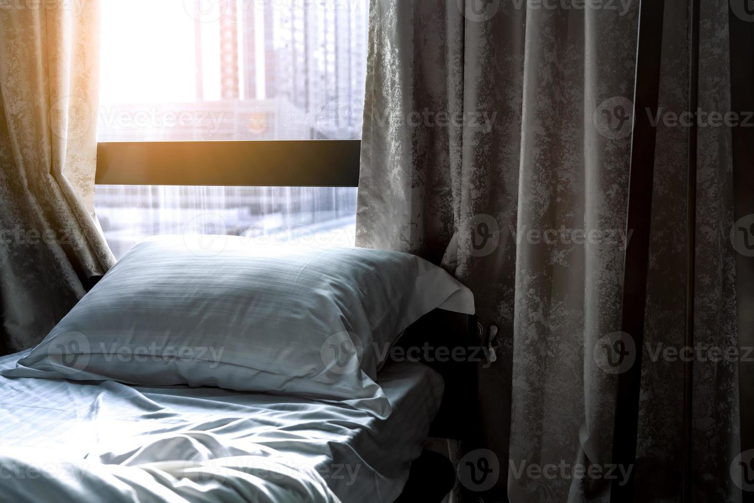 White comfort bed and soft pillow in modern bedroom. Bed near window and curtain at hotel in the morning with sunlight. Linen bed sheet and pillowcase. Bedroom interior design. Sleep with comfortable. photo