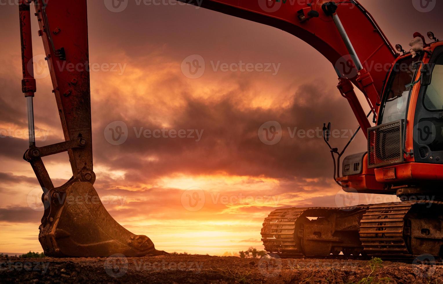 Backhoe parked at construction site after digging soil. Bulldozer on sunset sky and clouds background. Digger after work. Earth moving machine at construction site at dusk. Digger with old bucket. photo