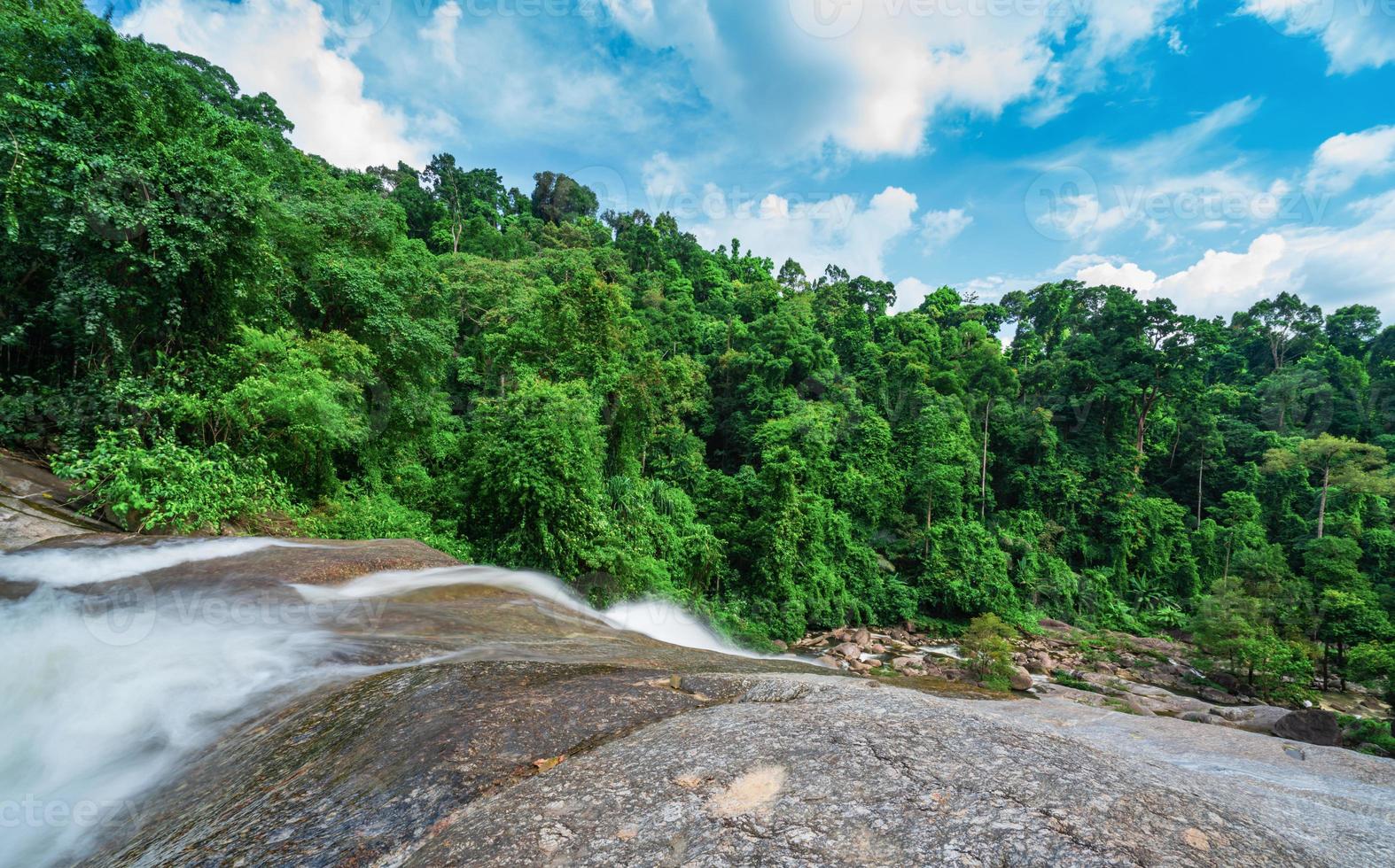 Beautiful waterfall at the mountain with blue sky and white cumulus clouds. Waterfall in tropical green tree forest. Waterfall is flowing in jungle. Nature abstract background. Granite rock mountain. photo