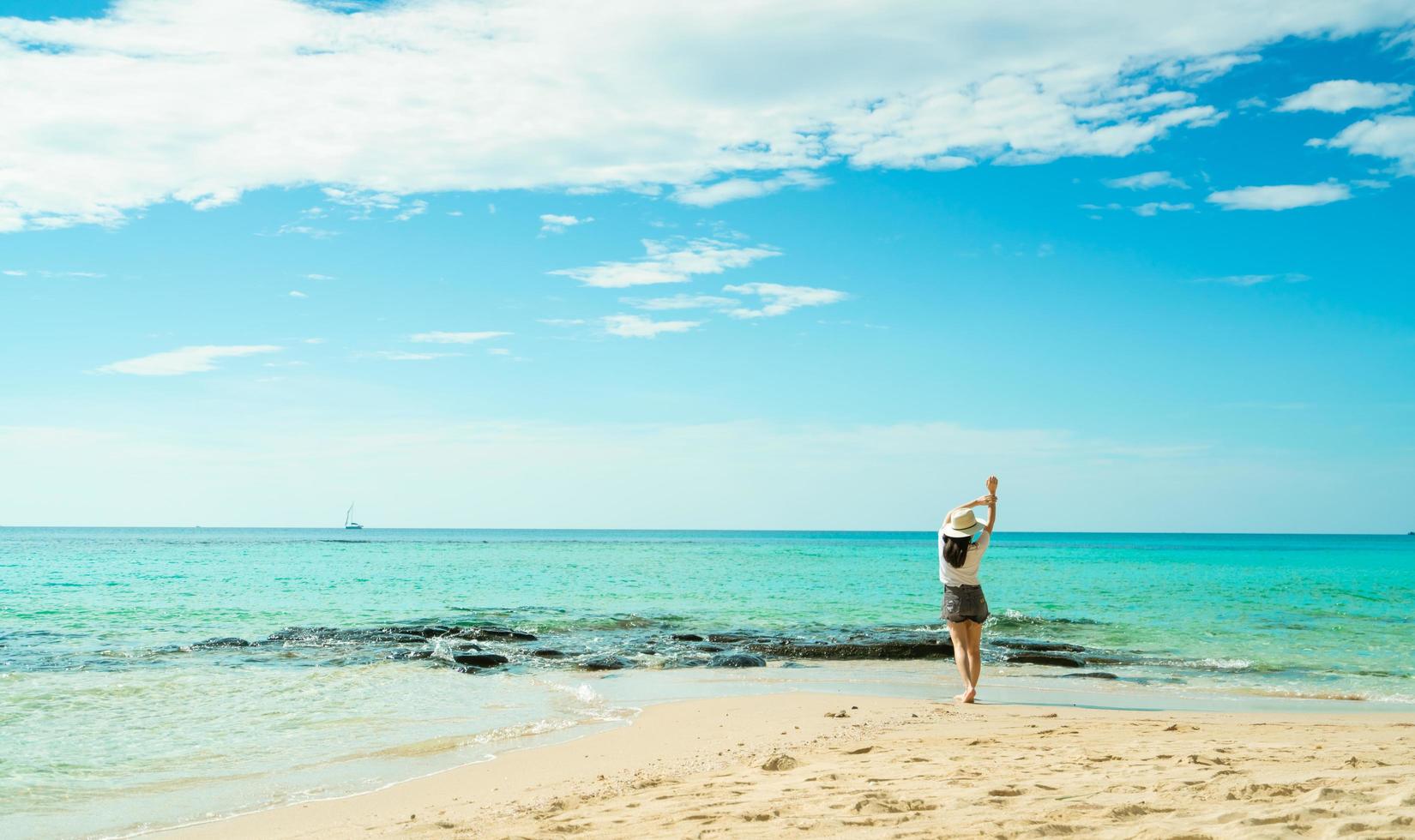 Happy young woman in white shirts and shorts walking at sand beach. Relaxing and enjoying holiday at tropical paradise beach with blue sky and clouds. Girl in summer vacation. Summer vibes. Happy day. photo