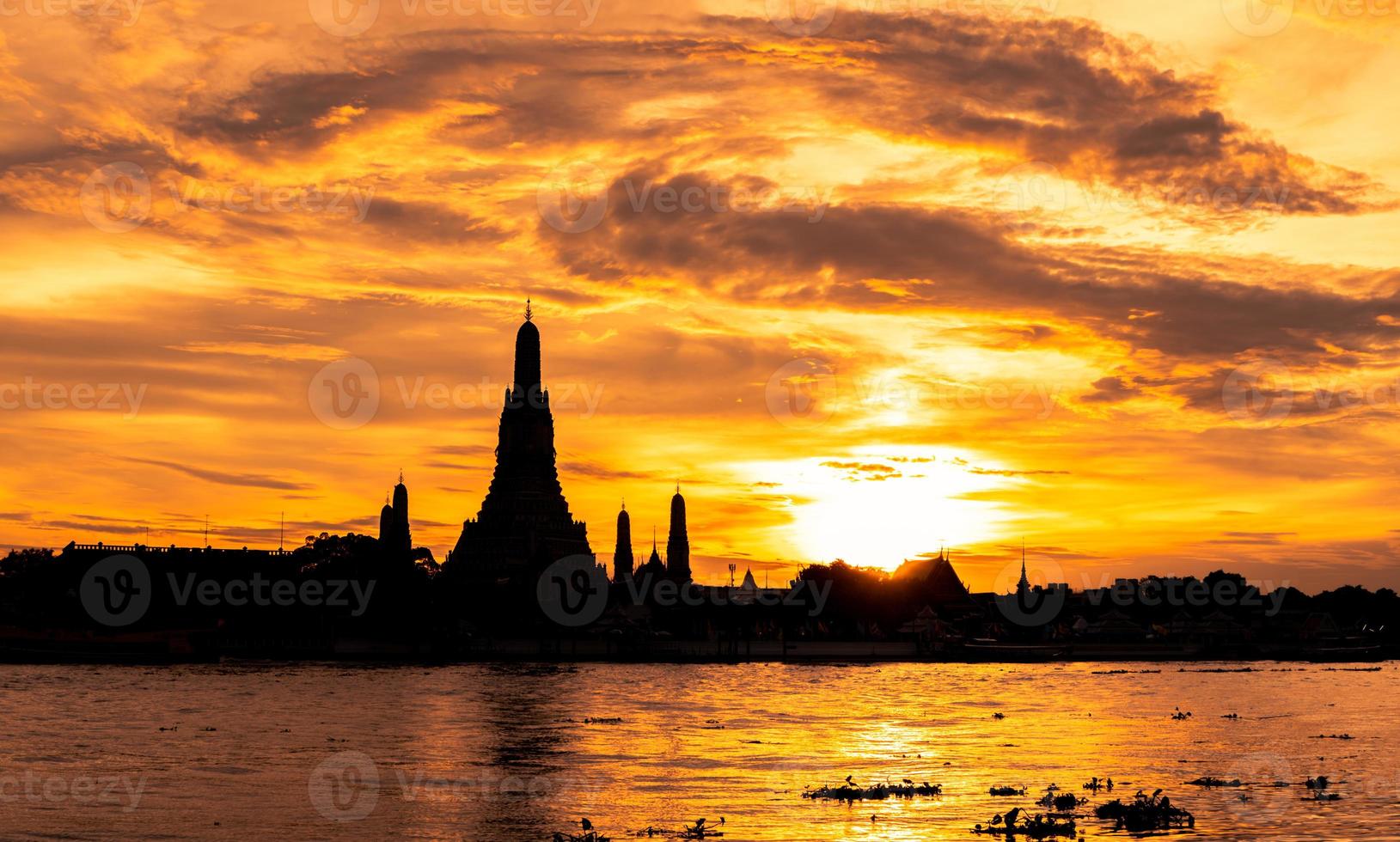 River and Wat Arun Ratchawararam at sunset with beautiful  orange sky and clouds. Wat Arun buddhist temple is the landmark in Bangkok, Thailand. Silhouette dramatic sky and temple in Thailand. photo