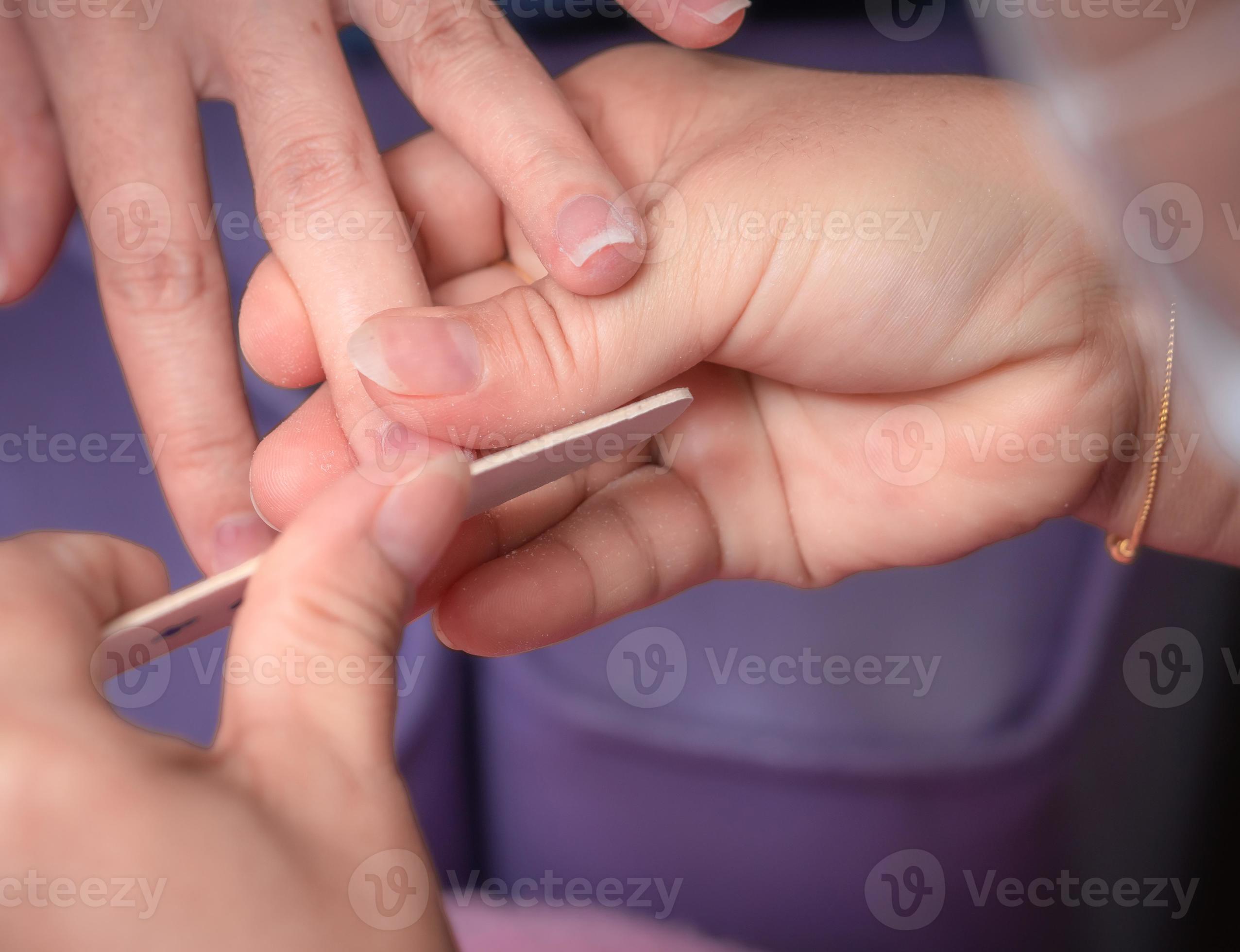 Woman receiving fingernail manicure service by professional manicurist at nail salon. Beautician