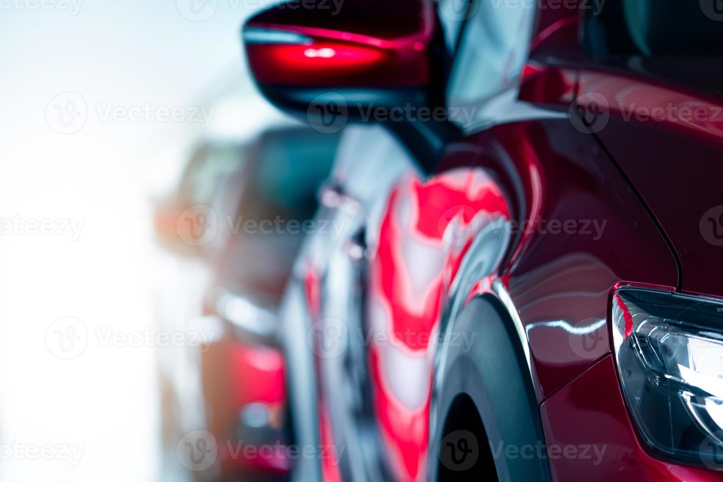 Closeup headlamp of red car parked in modern showroom. New and luxury car. Car dealership concept. Automotive industry. Automobile leasing. Front view of red shiny car parked in a row in showroom. photo