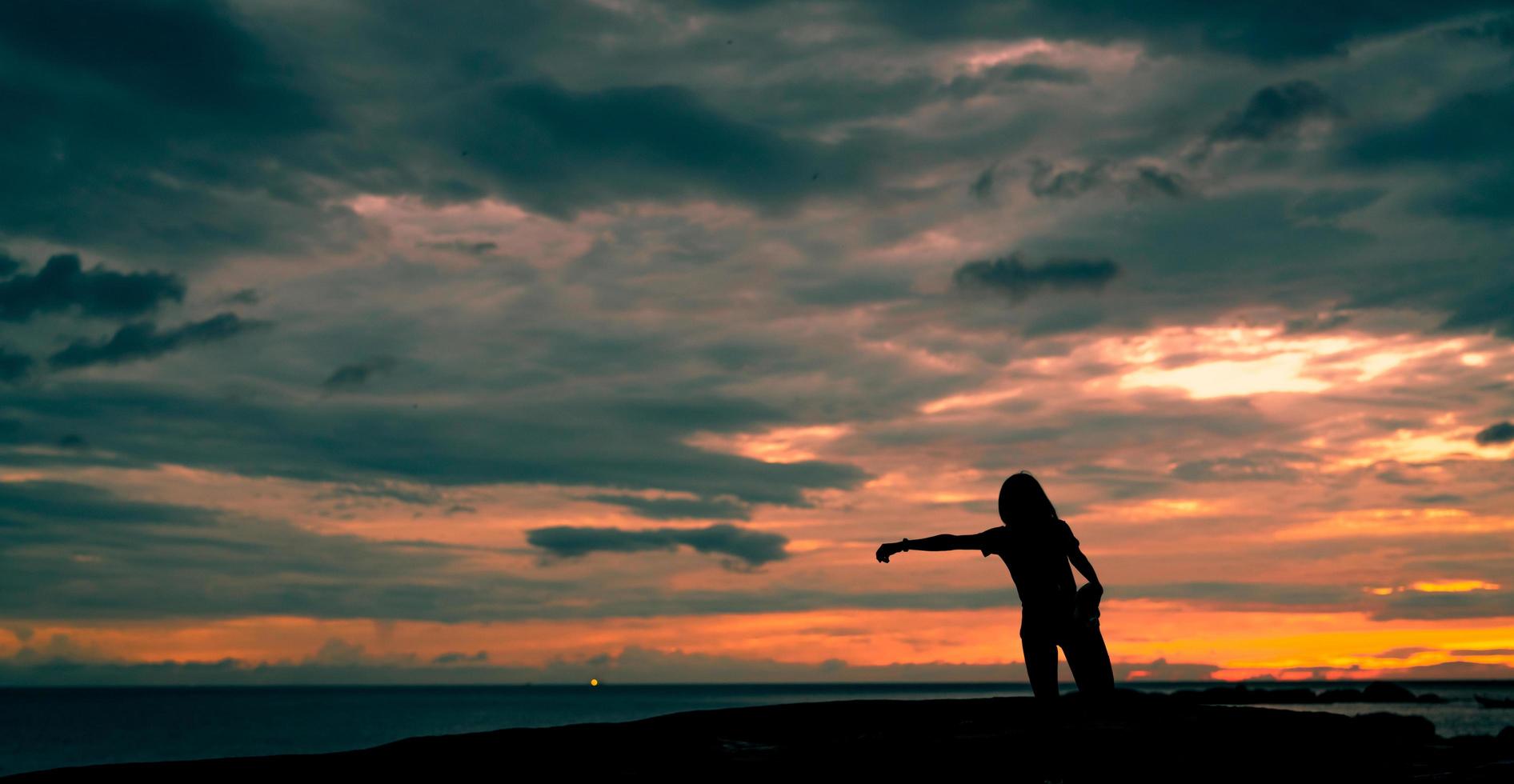 entrenamiento de mujer de silueta por la mañana en la playa de piedra con un hermoso cielo de amanecer. Corredor de mujer en forma estirando el cuerpo antes de correr. ejercicio cardiovascular para un estilo de vida saludable. chica activa entrenando sola. foto