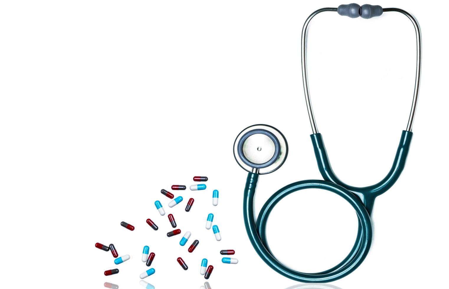 Green stethoscope and pile of capsule pills isolated on white background with copy space for text. Medical tool for doctor. Health check up concept. Medical equipment. Clinical Cardiology concept. photo