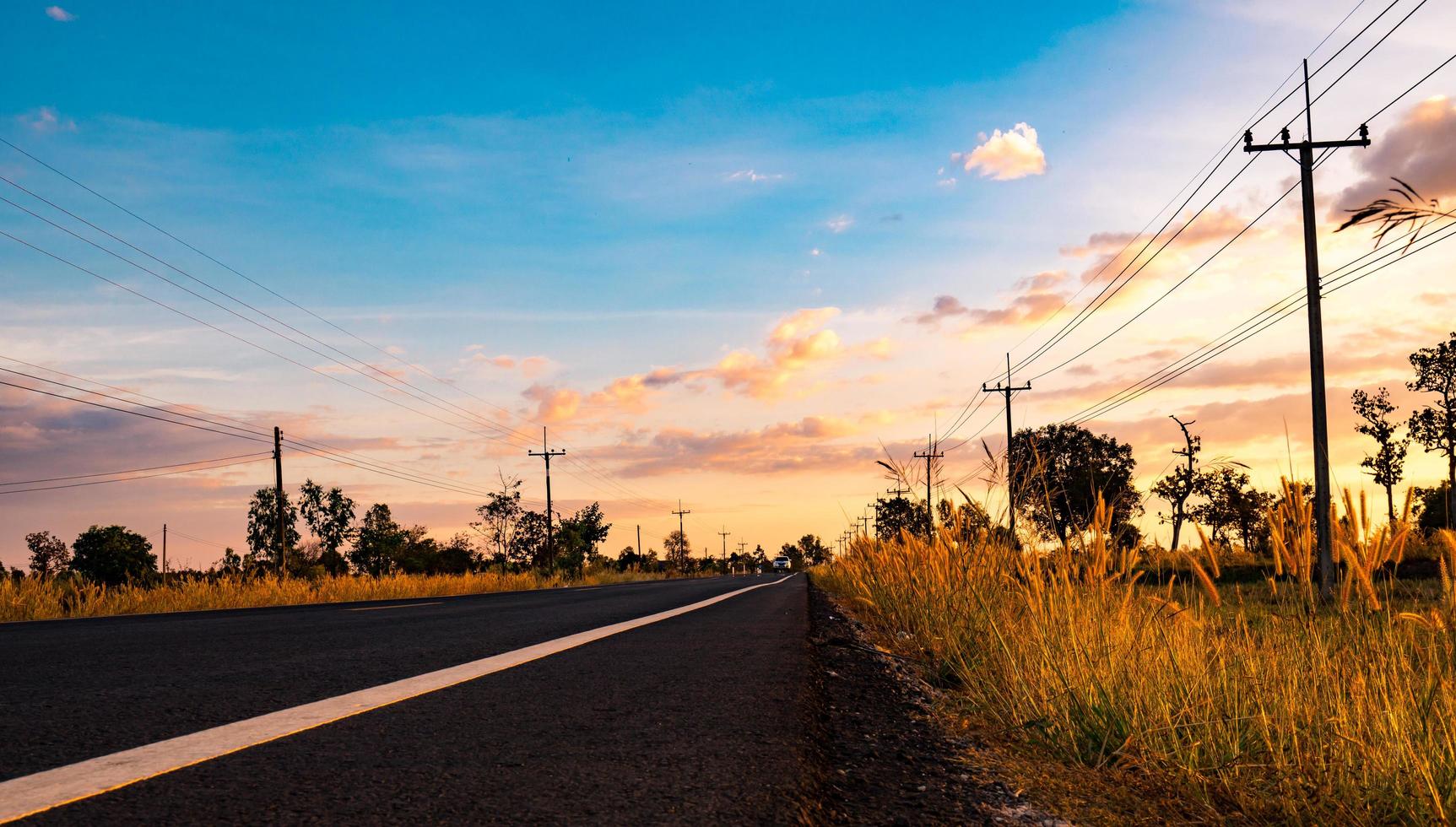 carretera asfaltada con poste eléctrico y prados en el camino. campo en tailandia foto