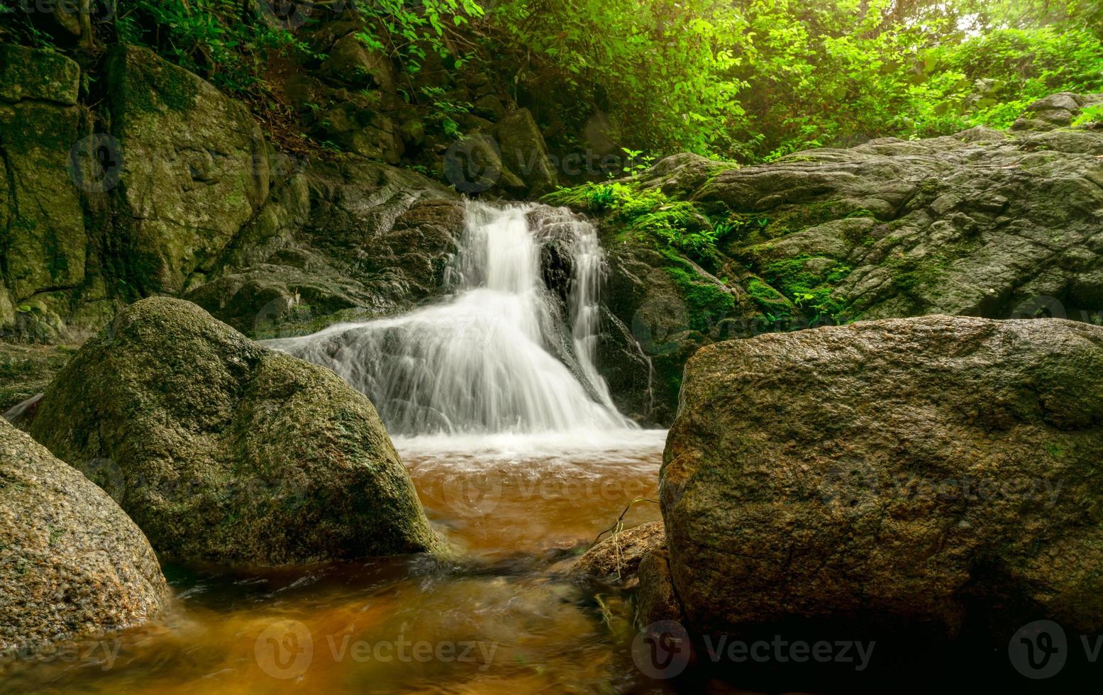 hermosa cascada en la selva. cascada en el bosque tropical con árboles verdes y luz solar. la cascada fluye en la jungla. fondo de la naturaleza. roca o piedra en cascada. viajes de temporada verde en tailandia foto