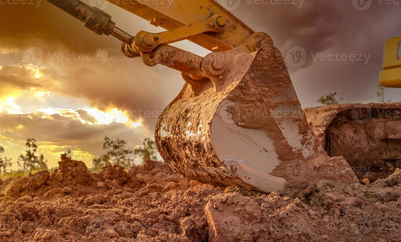 Dirt metal bucket of backhoe after digging soil. Backhoe parked at agricultural land on sunset sky background. Crawler excavator. Earthmoving machine at construction site at dusk. Excavation vehicle. photo