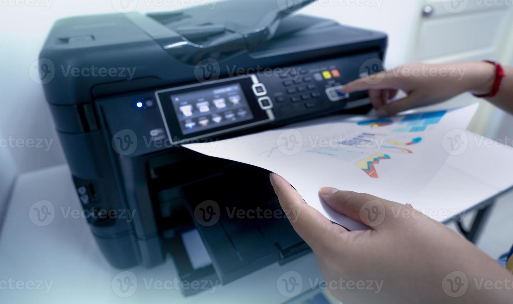 Office worker prints paper on multifunction laser printer. Copy, print, scan, and fax machine in office. Document and paper work. Print technology. Hand press on photocopy machine and holding paper. photo