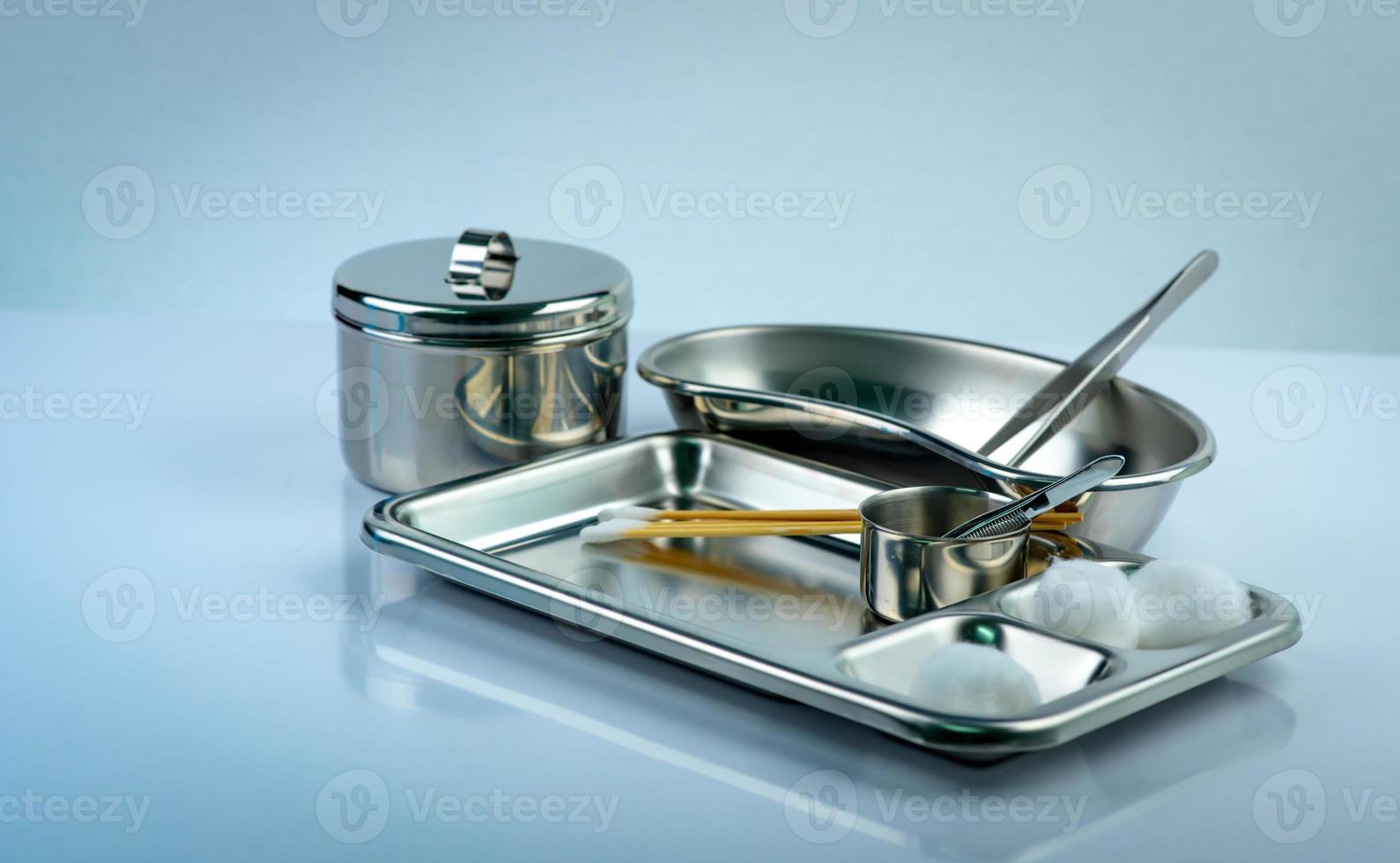 Wound care dressing set on stainless steel plate. White cotton ball, cotton stick, forceps, kidney basin, iodine cup, instruments container  with cover or stainless steel cotton jar set. Medical tool. photo