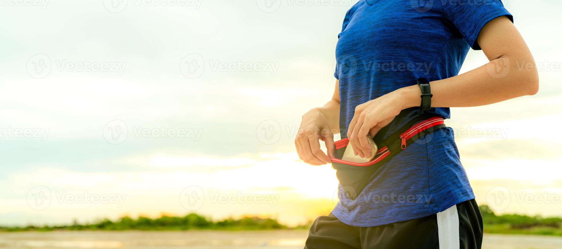 la joven asiática mantiene el teléfono inteligente en la riñonera antes de hacer ejercicio cardiovascular por la mañana. entrenamiento al aire libre corredor y dispositivo portátil de banda inteligente. gadget para un estilo de vida saludable. moda para correr. foto