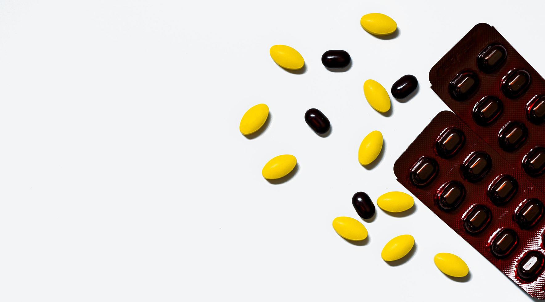 Macro shot of yellow oval tablet pills, black tablets pills on white background with creative pattern and black caplets pills in brown blister pack. Prepare pills before traveling abroad. photo