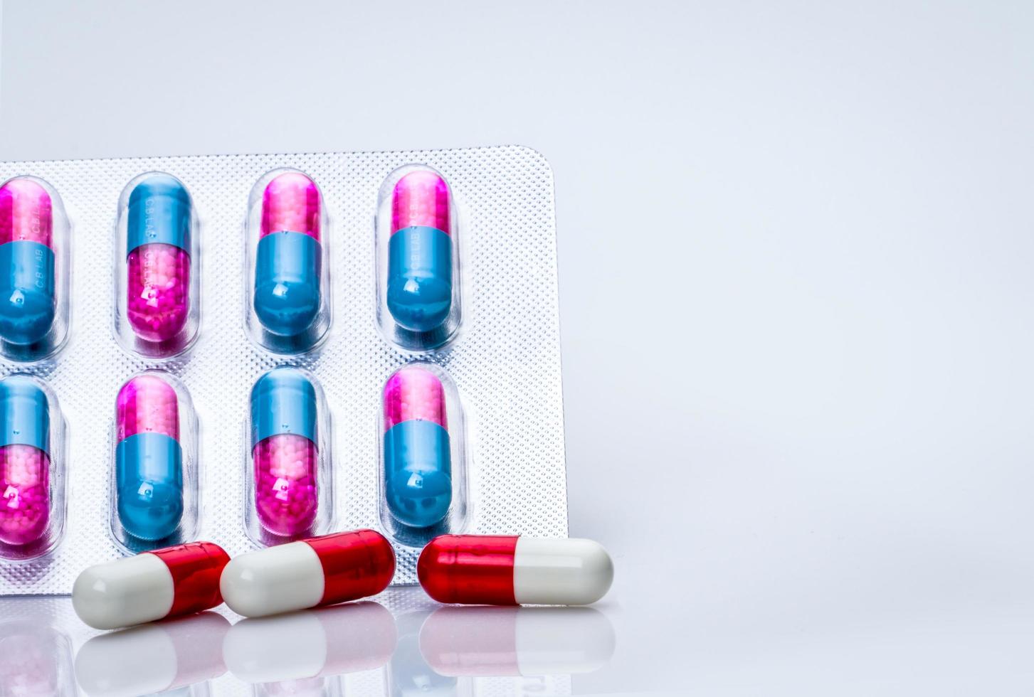 Red-white antibiotic capsule pills and pink-blue anti-fungal granules in capsule pills in blister pack on white background Antibiotics drug resistance and antimicrobial drug use with reasonable. photo