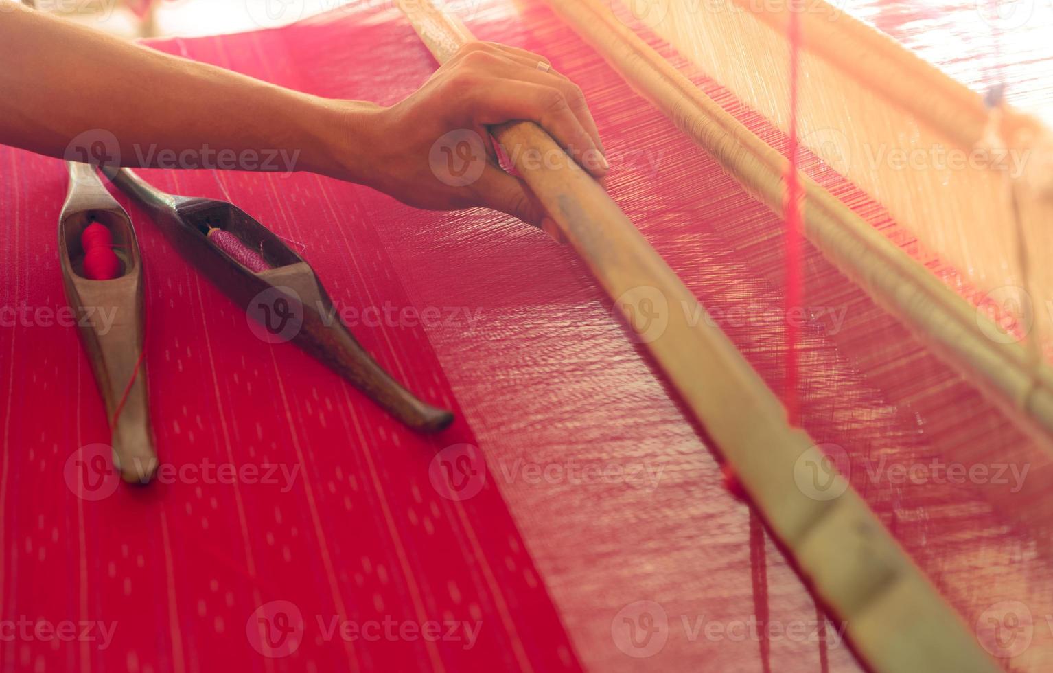 Woman working on weaving machine for weave handmade fabric. Textile weaving. Weaving using traditional hand weaving loom on cotton strands. Textile or cloth production in Thailand. Asian culture. photo