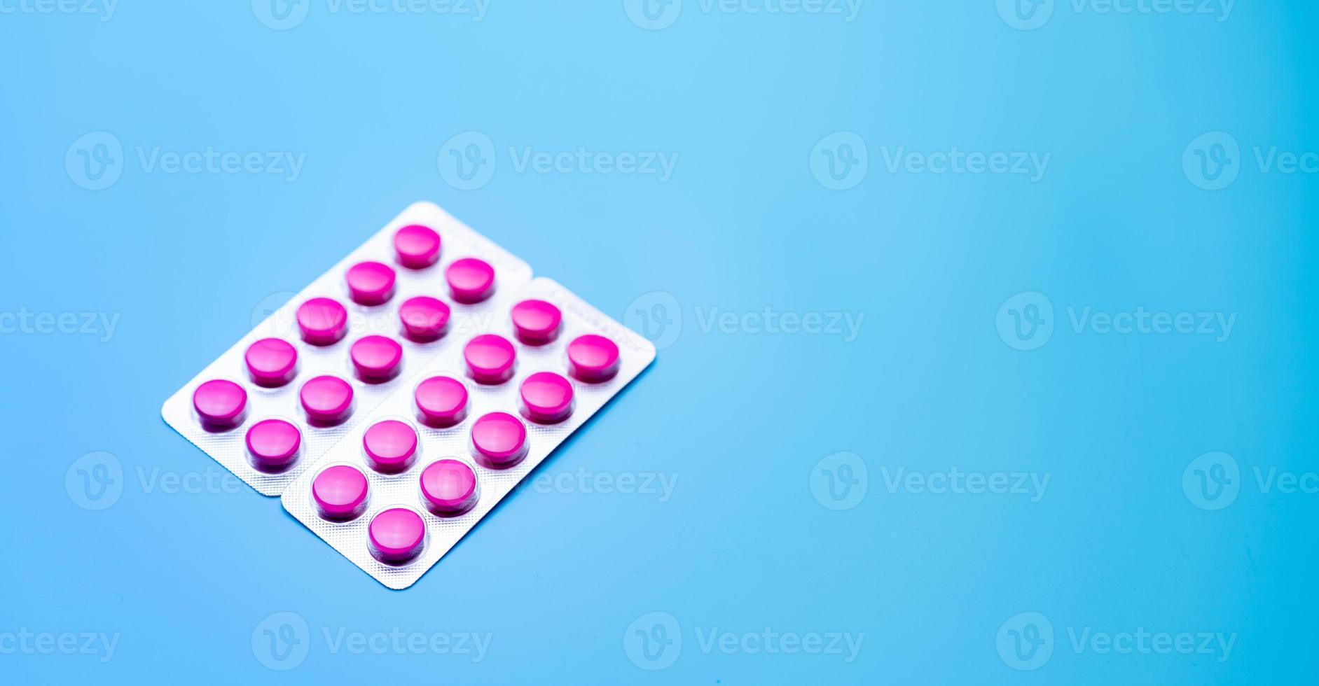 Round pink tablets pills in blister pack on blue background with space for text. Painkiller medicine. Online pharmacy and pharmacy web banner. Migraine headache and menstrual pain treatment pills. photo