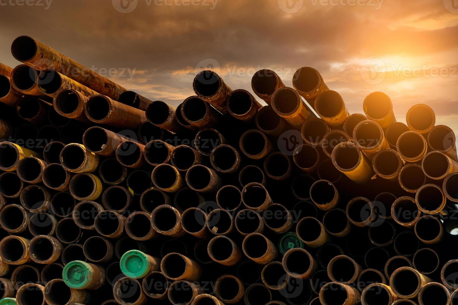 Pile of old rusty round metal industrial pipe. Steel pipe stack during sunset. Industrial material. Metal corrosion. Stack of round rusty tube abstract background. Old iron pipe warehouse of factory photo