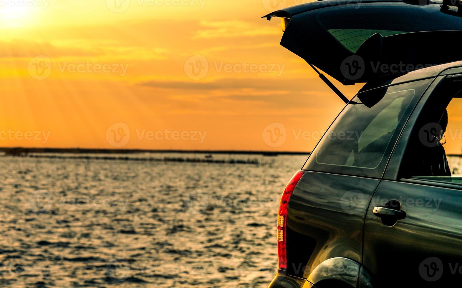 Black compact SUV car with sport and modern design parked on concrete road by the sea at sunset. Environmentally friendly technology. Road trip travel on vacation at the beach and open car truck photo