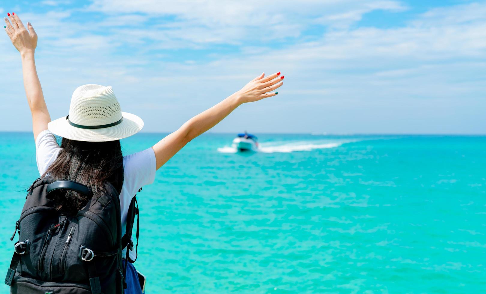 mujer asiática joven feliz en estilo casual con sombrero de paja y mochila. relájese y disfrute de unas vacaciones en la playa del paraíso tropical. chica de pie en el muelle de madera del resort en vacaciones de verano. vibras de verano. foto