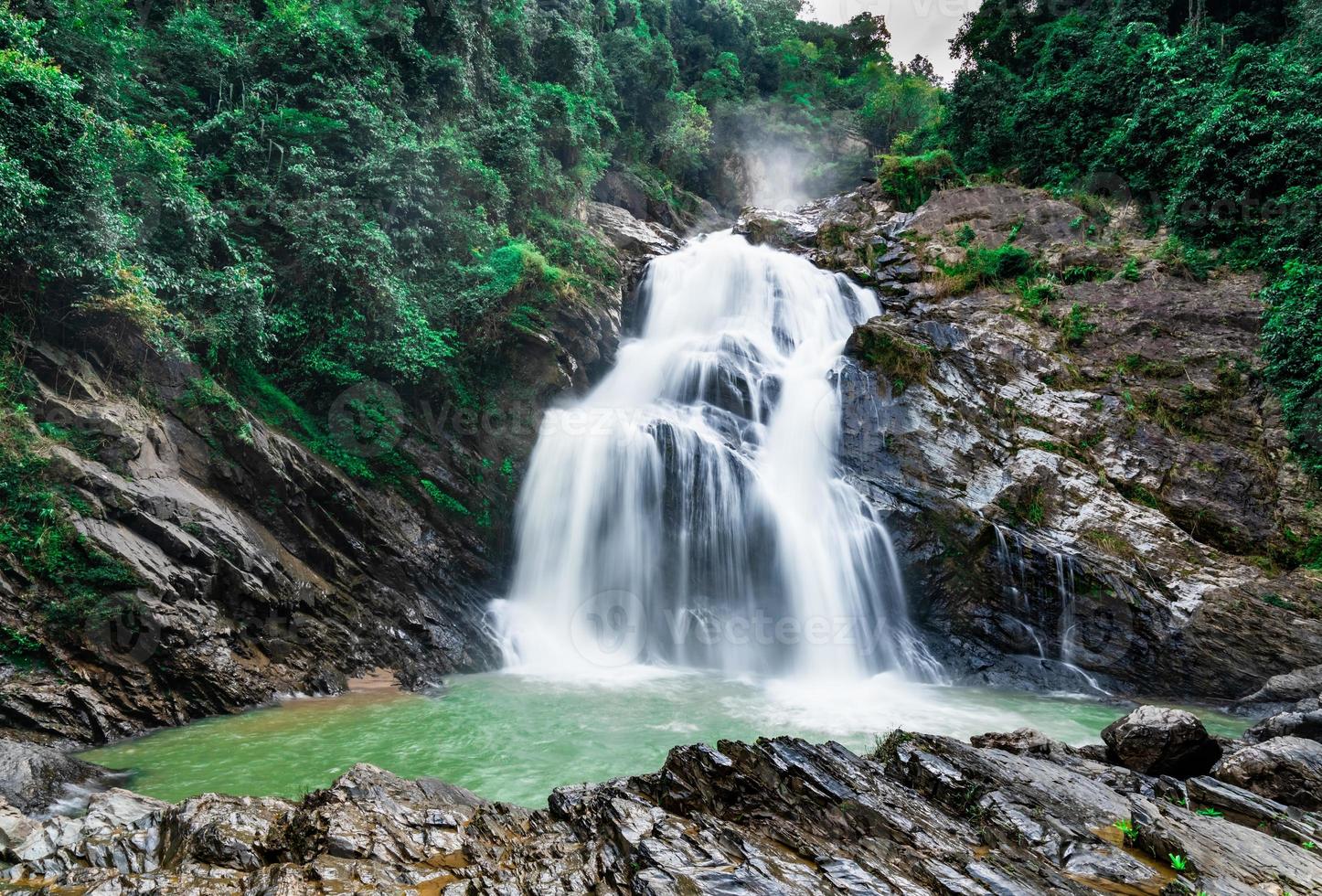 Beautiful waterfall at the mountain with blue sky and white cumulus clouds. Waterfall in tropical green tree forest. Waterfall is flowing in jungle. Nature abstract background. Granite rock mountain. photo