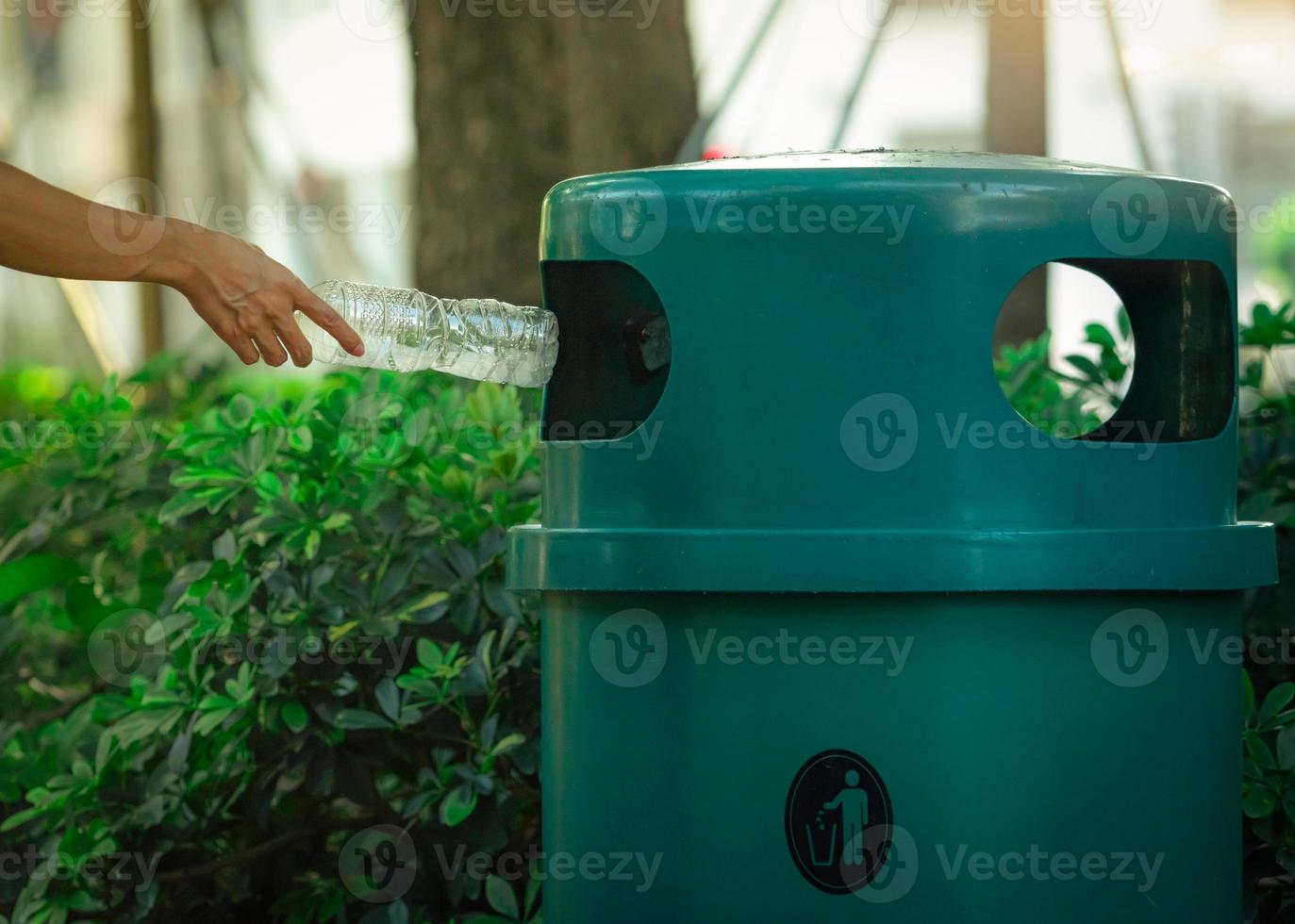 People hand throwing empty water bottle in recycle bin at park. Green plastic recycle bin. Man discard bottle in trash bin. Waste management. Plastic bottle garbage. Reduce and reuse plastic concept. photo