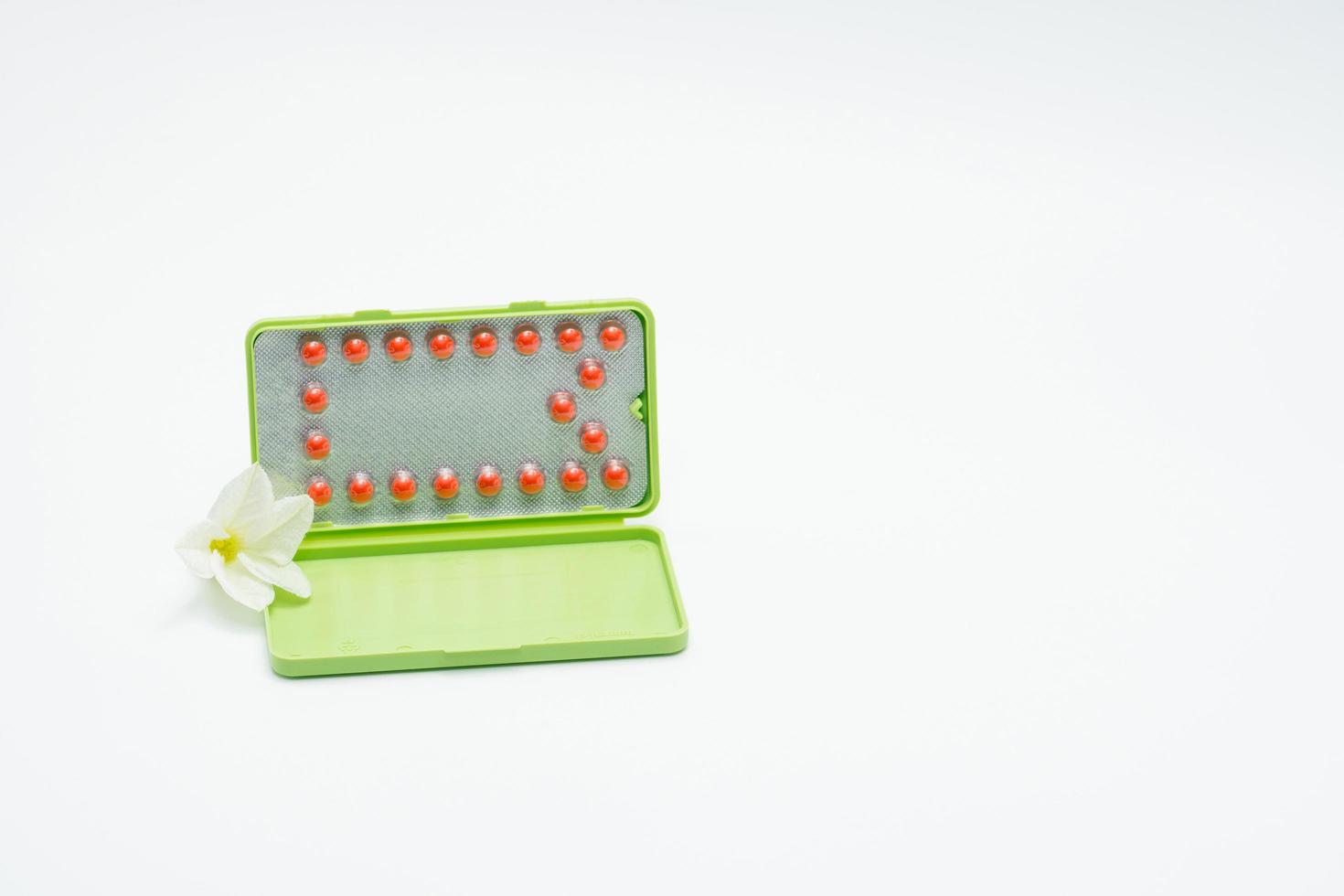 Birth control pills or contraceptive pill with paper case and white flower on white background. Family planning concept. Hormone replacement therapy. Hormonal acne treatment with anti-androgenic pill. photo