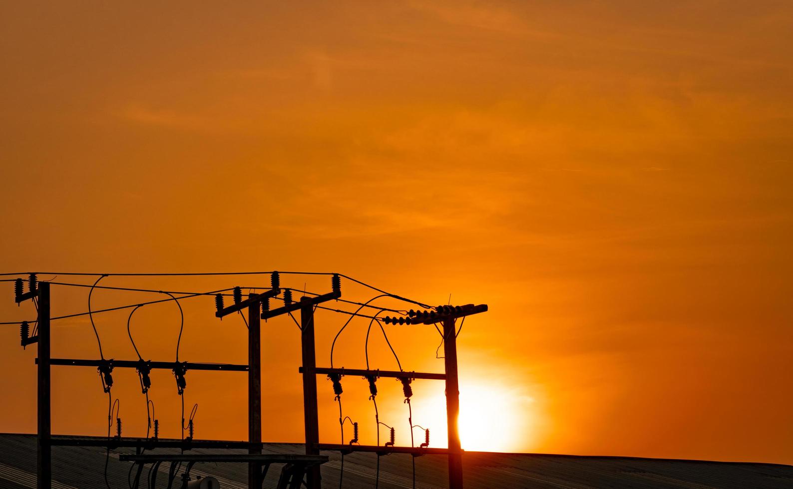 Three-phase electric power for transfer power by electrical grids. High voltage electric poles in factory and roof of building and orange sunset sky. Electric power for support manufacturing industry. photo