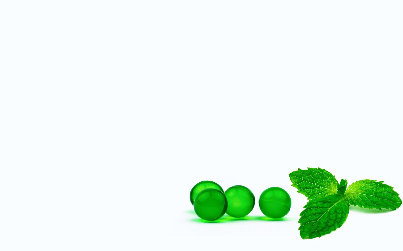 Green round soft capsule pills and mint leaves isolated on white background with copy space. Ayurvedic medicine for indigestion, gas and acidity. Herbal medicine from India. Asia herbal medicine. photo