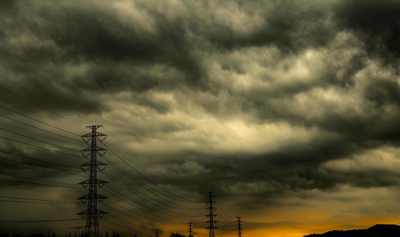 Dramatic dark sky and clouds and high voltage pole with electric cable. Cloudy sky background. Black sky before thunder storm. Background for sad, grieving or depression. Electric tower at industrial. photo