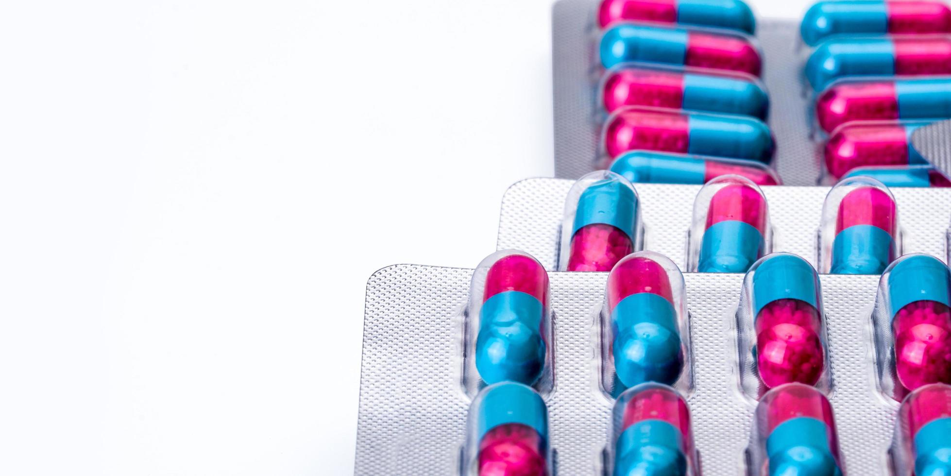 Colorful of blue pink capsule with granule in side pills. Pills in blister pack on white background with space. Pharmaceutical dosage form and packaging. Itraconazole 100 mg  Anti fungal medicine. photo
