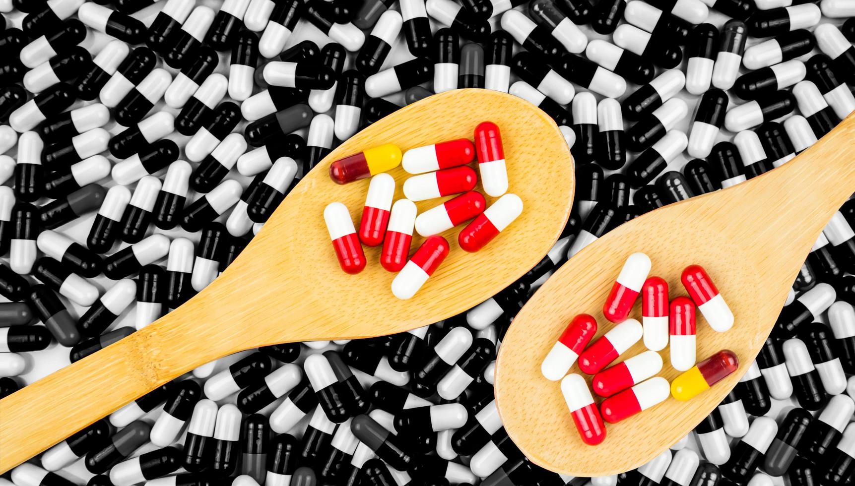 Colorful of antibiotics capsule pills in wooden spoon on black and white background of capsules. Drug resistance concept. Antibiotics drug use with reasonable and global healthcare concept. photo